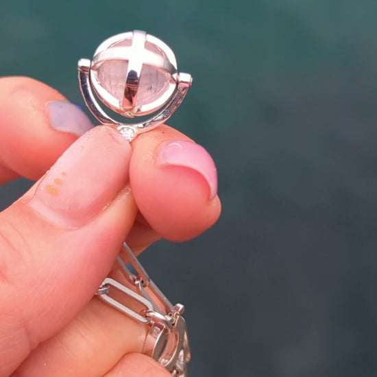 Silver ORB necklace held in a hand while the cage containing the rose quartz sphere is turned and spun by hand.