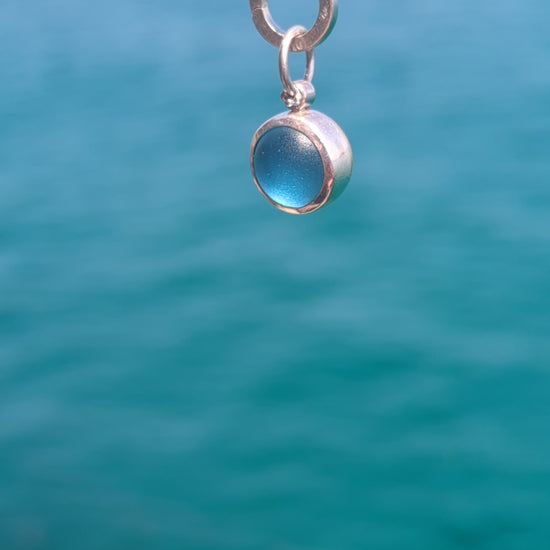 Video of the handmade blue sea glass pendant showing its rounded back designed to roll and catch the light.