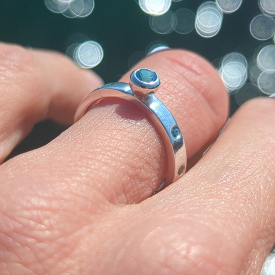 video of Silver ring with Swiss blue topaz and blue cubic zirconia gemstones on a hand with shimmering ocean in background made by Booblinka Jewellery