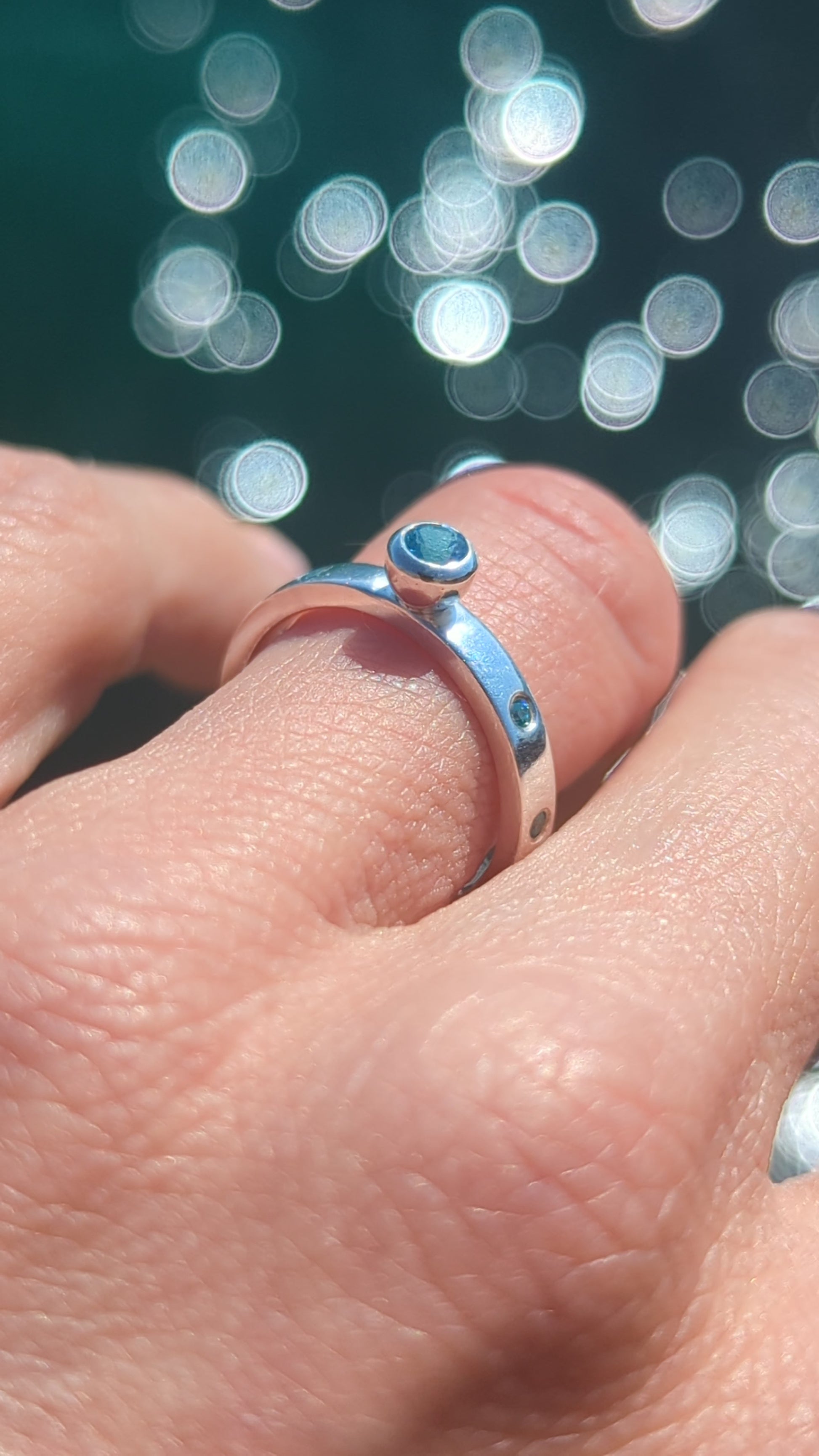 video of Silver ring with Swiss blue topaz and blue cubic zirconia gemstones on a hand with shimmering ocean in background made by Booblinka Jewellery