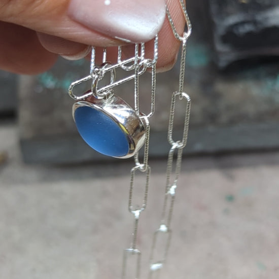 Video showing a handmade cornflower blue sea glass necklace in sterling silver with a sparkling paperclip chain.