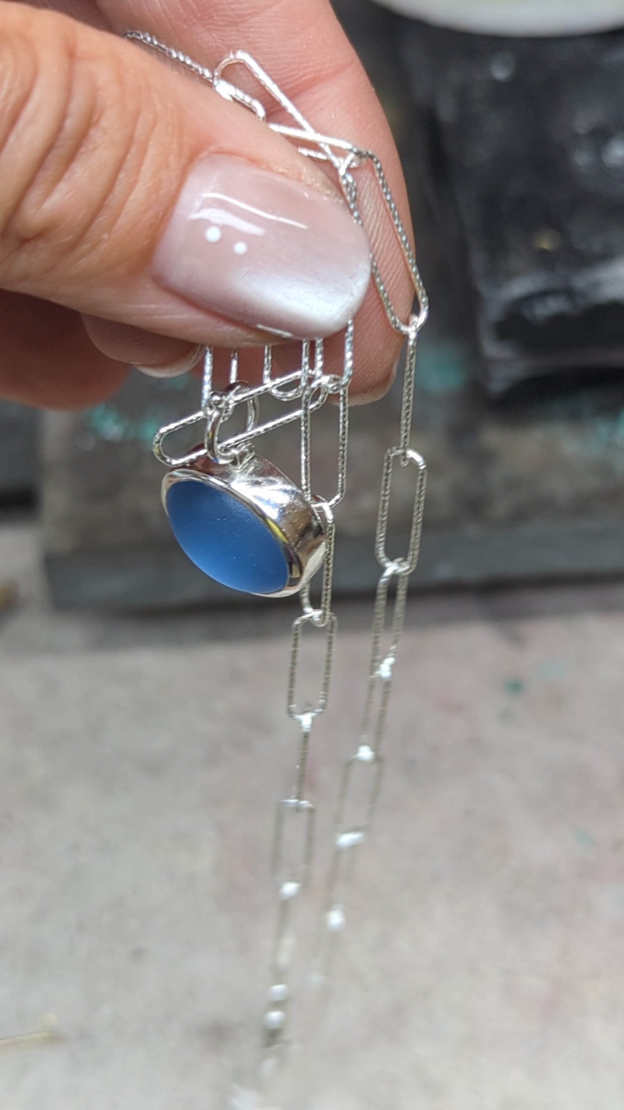 Video showing a handmade cornflower blue sea glass necklace in sterling silver with a sparkling paperclip chain.