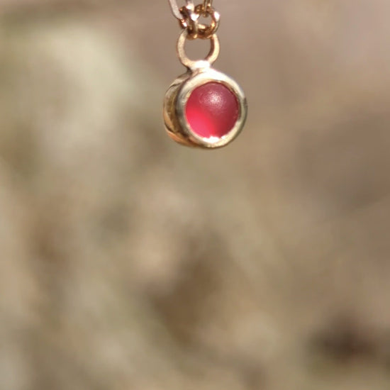 Red sea glass necklace in 9ct gold catching light in natural sunlight