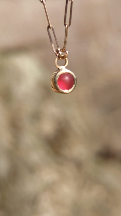 Red sea glass necklace in 9ct gold catching light in natural sunlight