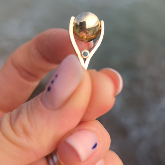 9ct gold spinning mini pendant showing how it spins above the ocean between fingers made by Booblinka Jewellery.