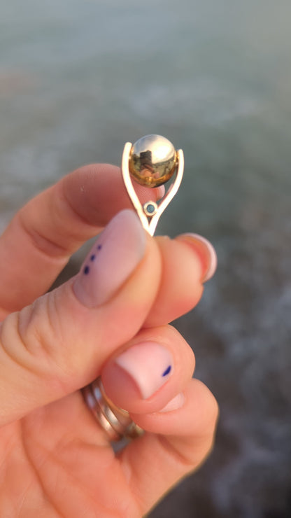 9ct gold spinning mini pendant showing how it spins above the ocean between fingers made by Booblinka Jewellery.