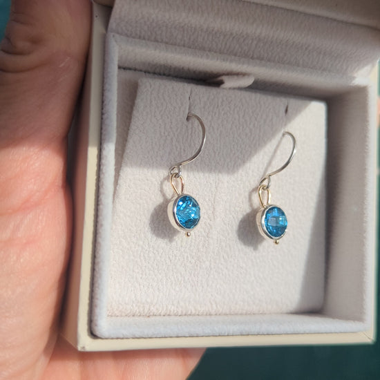 video of Pair of Swiss blue topaz dangle earrings in sterling silver and 9ct gold, photographed beside the blue ocean in Cornwall.