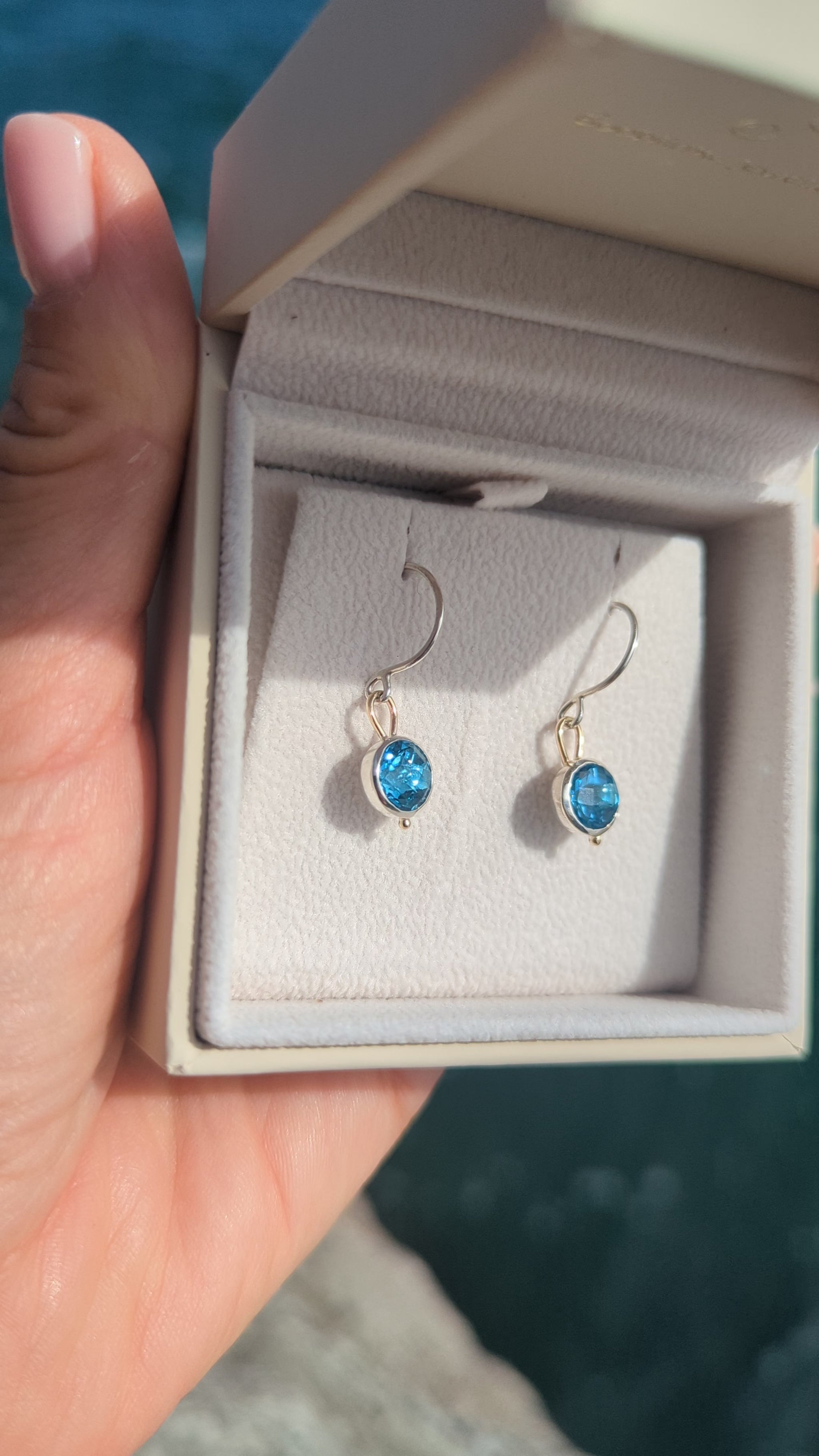 video of Pair of Swiss blue topaz dangle earrings in sterling silver and 9ct gold, photographed beside the blue ocean in Cornwall.