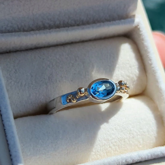 Detail of handmade silver Ring with a Swiss blue oval topaz and gold granules in a plush jewellery box made by Booblinka Jewellery