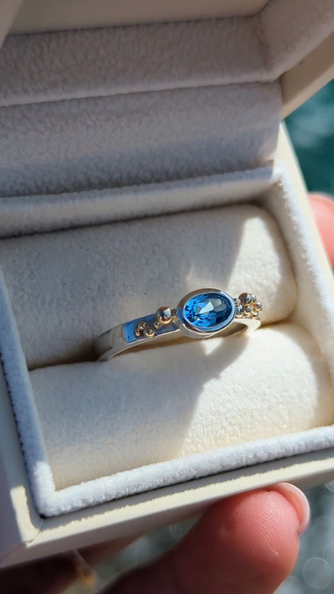 Detail of handmade silver Ring with a Swiss blue oval topaz and gold granules in a plush jewellery box made by Booblinka Jewellery