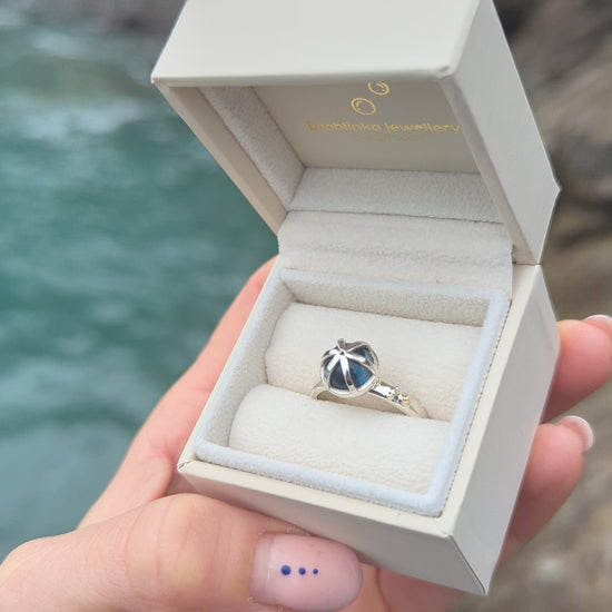 Video of statement silver ring with London blue topaz and gold granules in a jewellery box held in hand above the ocean made by Booblinka Jewellery
