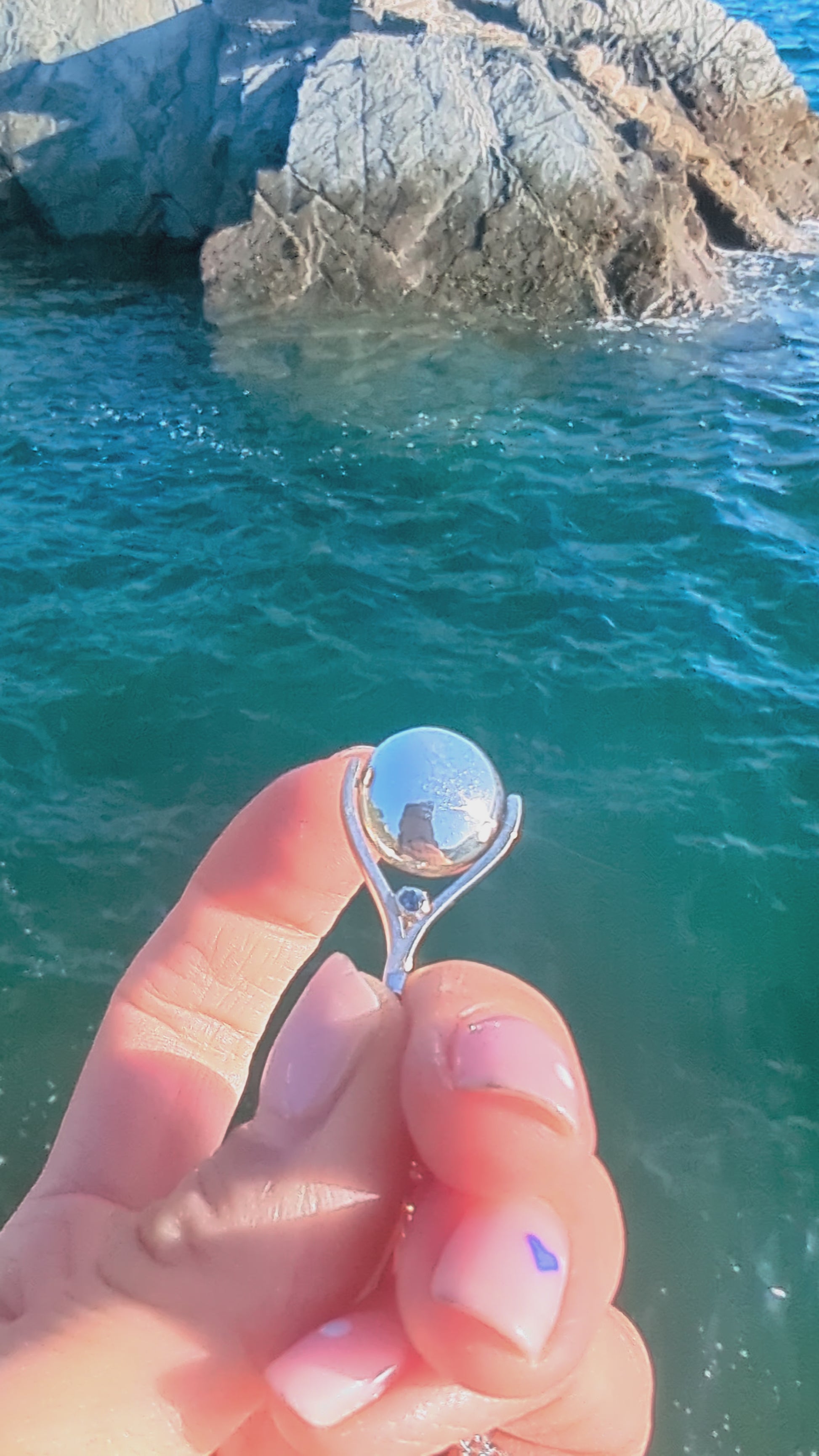 Video of silver spinning necklace with blue topaz spinning above the ocean made by Booblinka Jewellery.