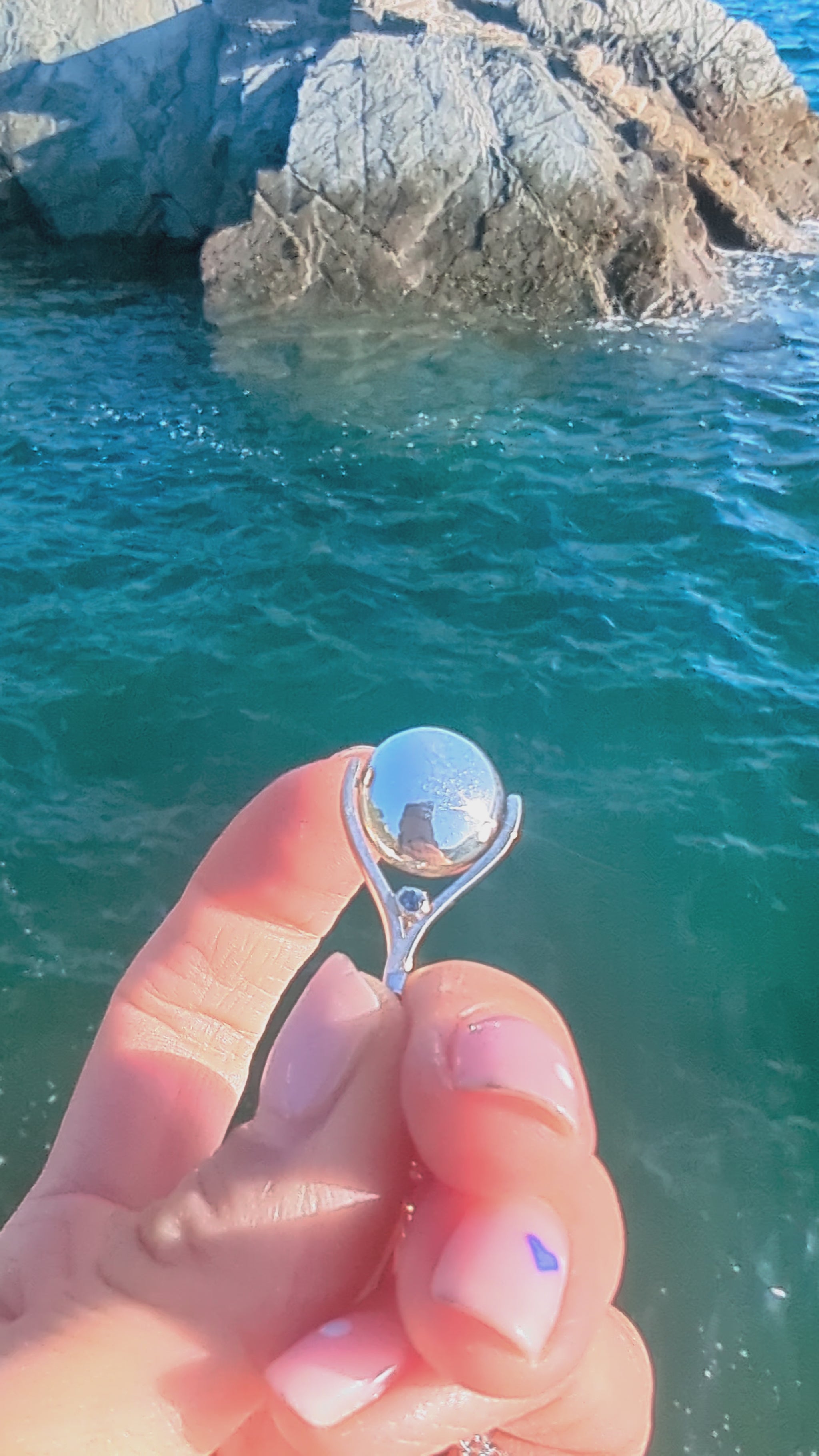 Video of silver spinning necklace with blue topaz spinning above the ocean made by Booblinka Jewellery.