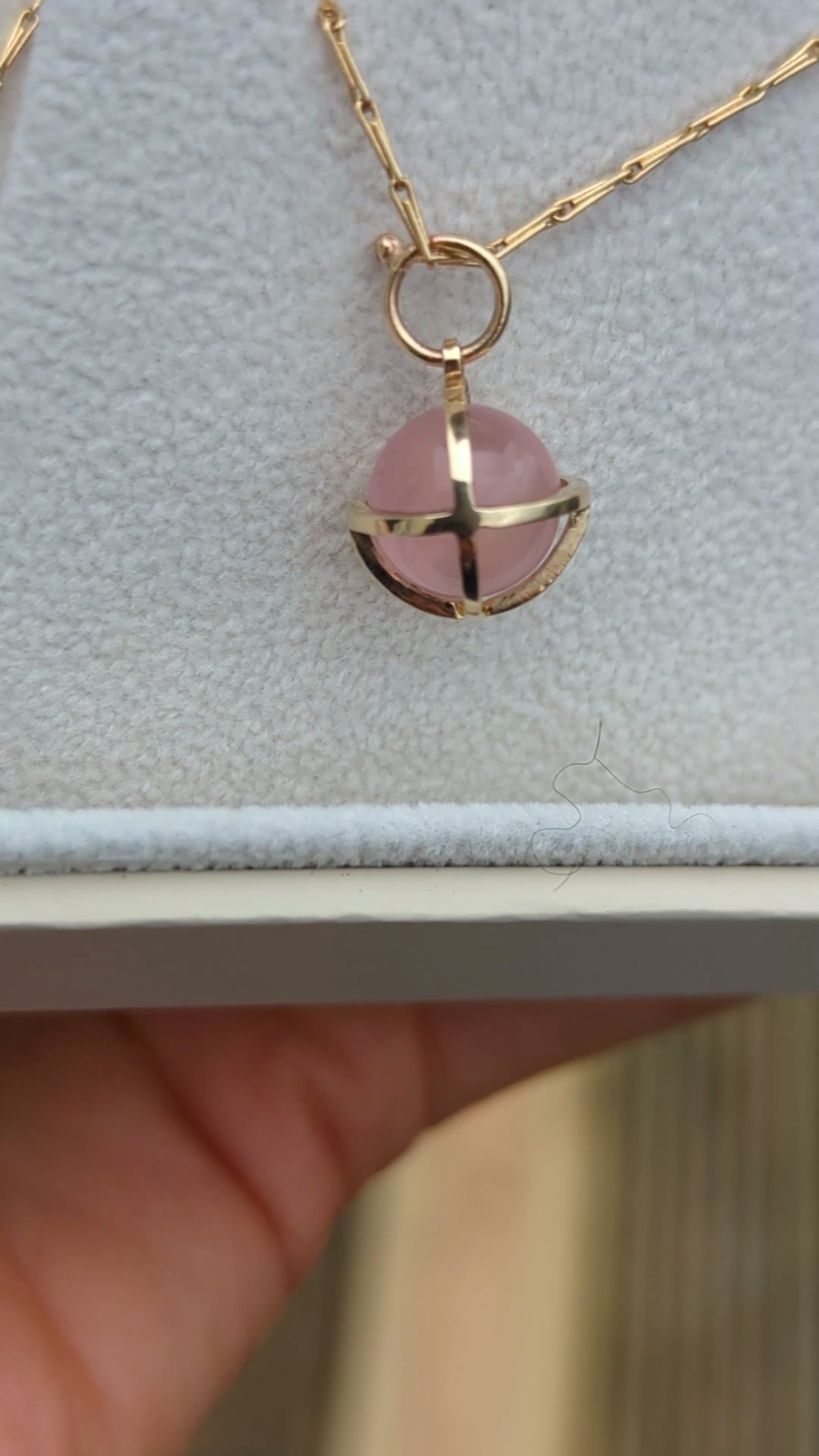 Video of spherical rose quartz set in solid gold cage in a jewellery box