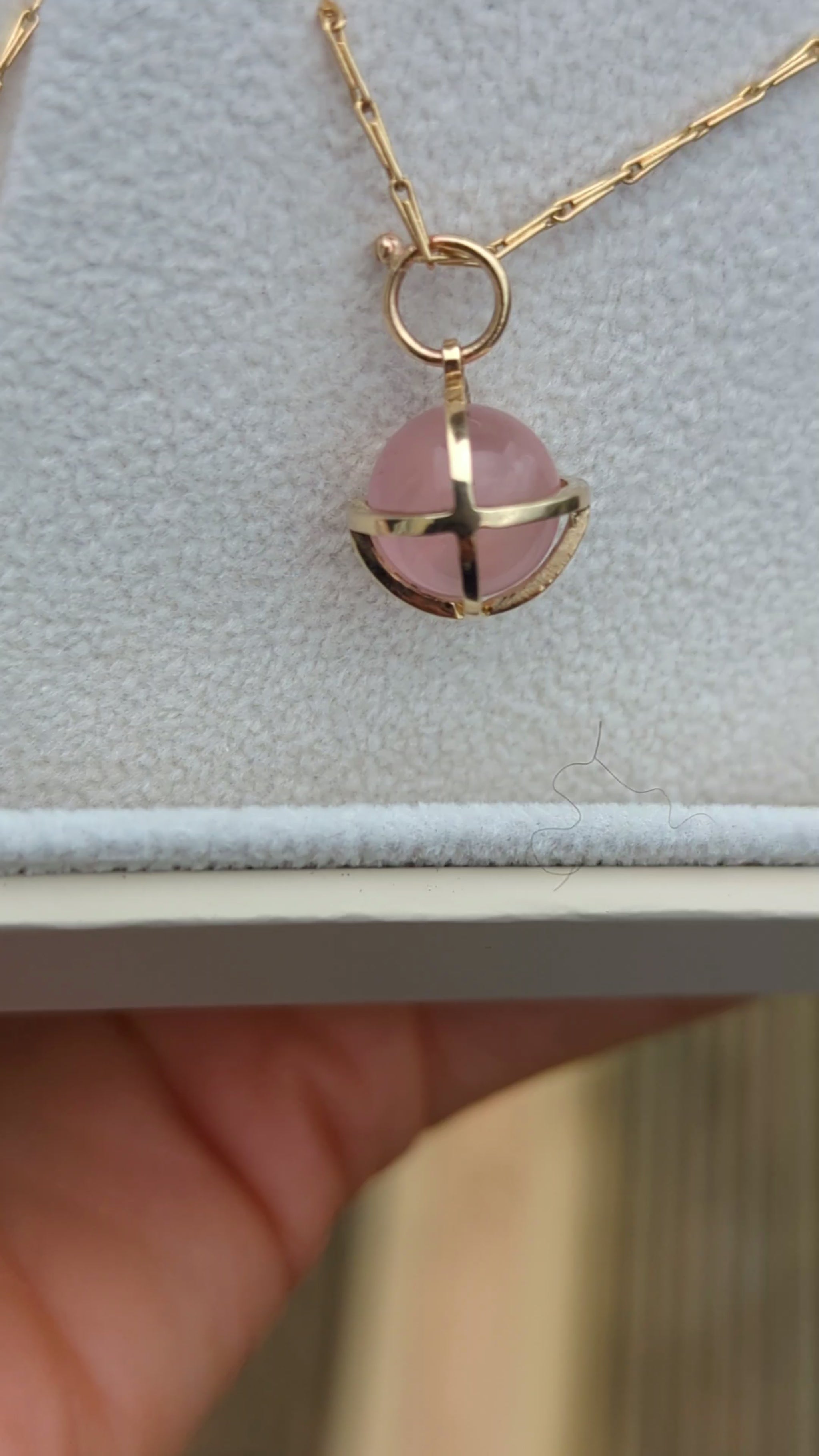 Video of spherical rose quartz set in solid gold cage in a jewellery box