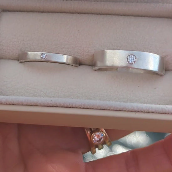 Video showing the two sterling silver wedding bands with flush-set moissanites in an open jewellery box with blurred ocean background.