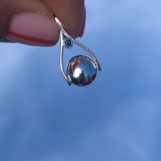 video showing mini silver spinning necklace with blue diamond spinning between fingers