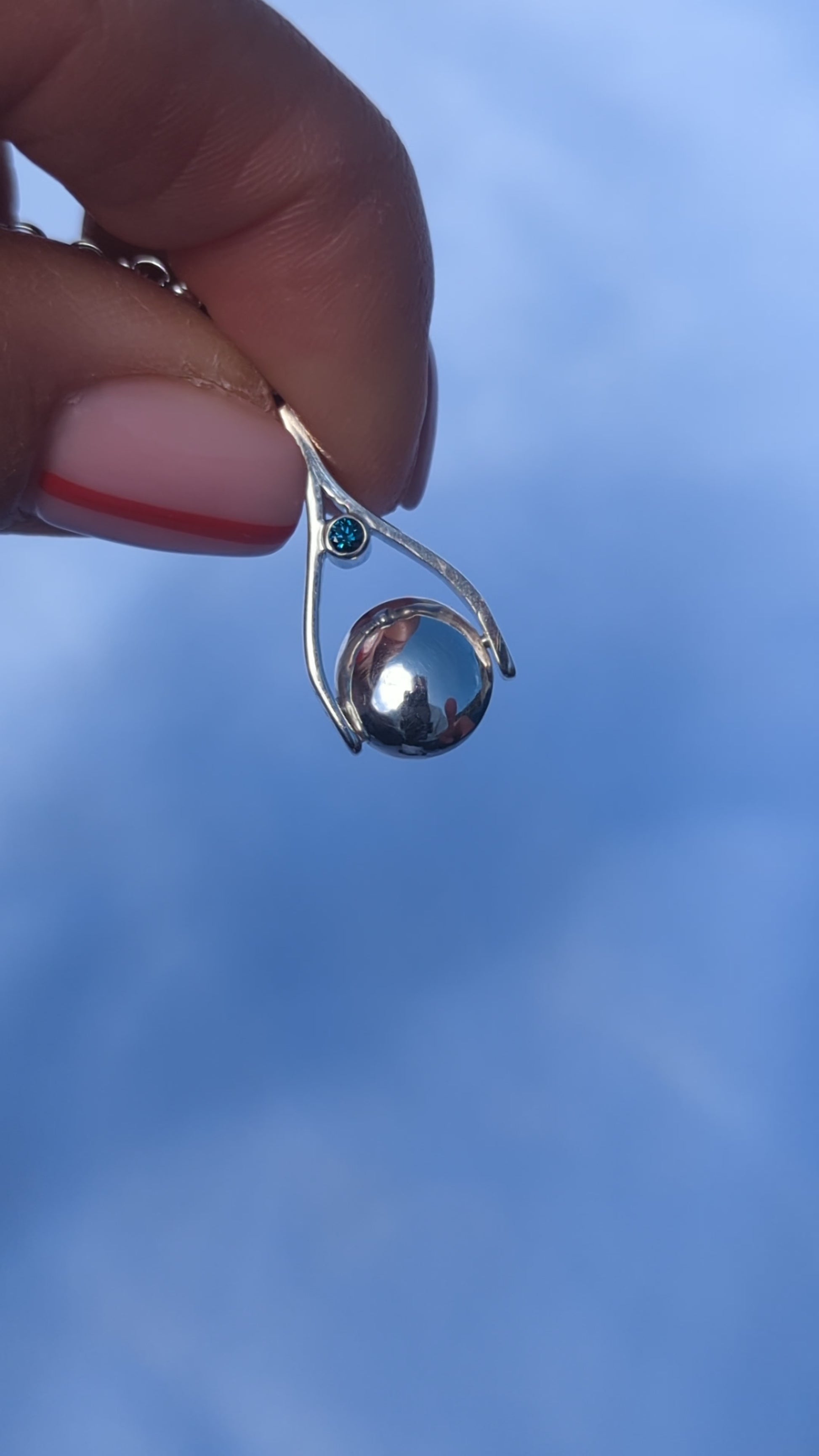 video showing mini silver spinning necklace with blue diamond spinning between fingers