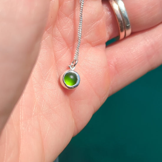 Video showing a tiny genuine green sea glass necklace in sterling silver held in the hand to show its size and colour.