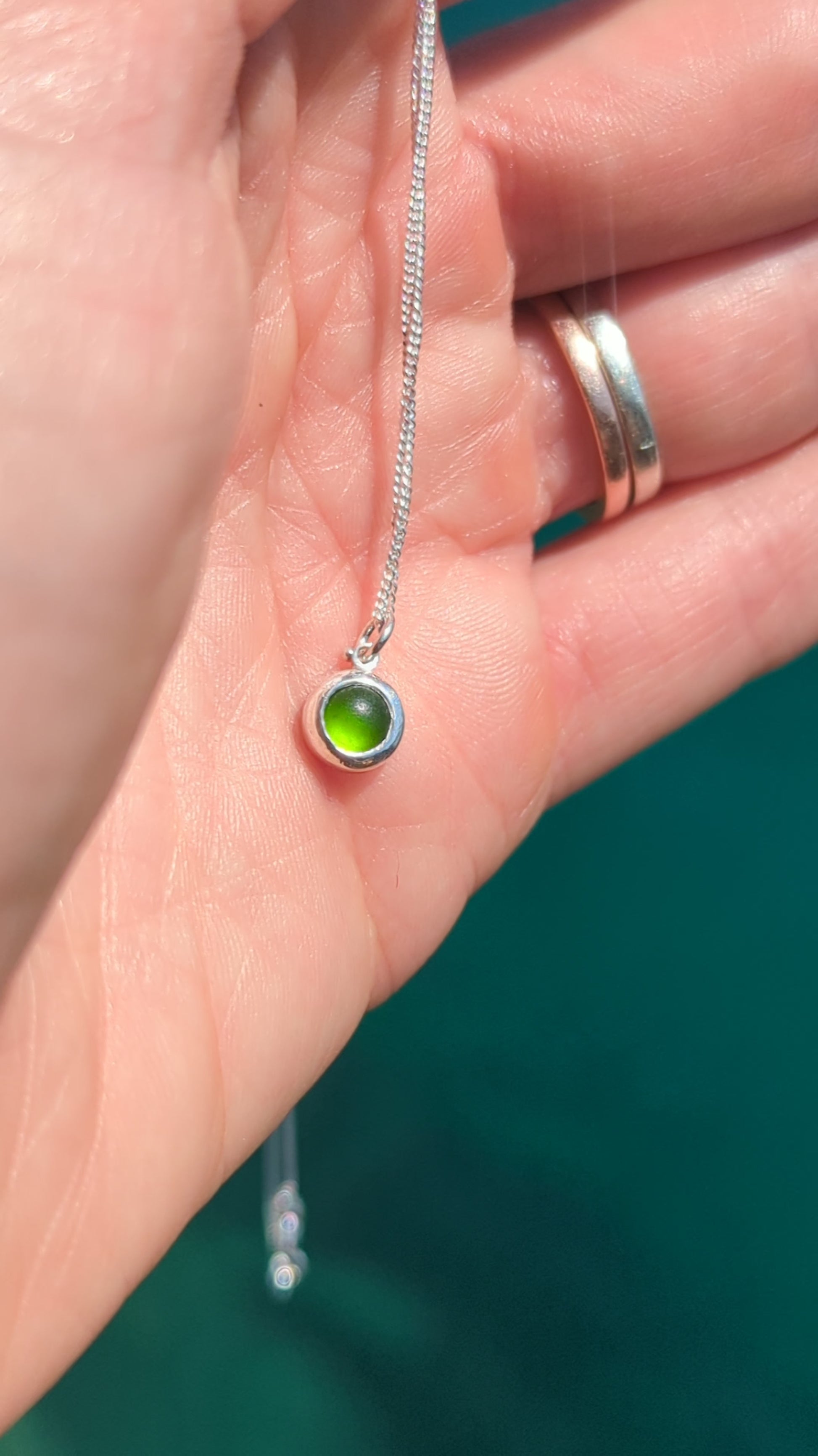 Video showing a tiny genuine green sea glass necklace in sterling silver held in the hand to show its size and colour.