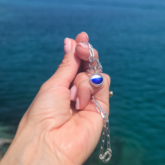 Video of a handmade blue and white sea glass pendant showing the colours and sterling silver setting above the ocean.