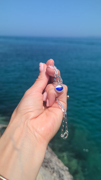 Video of a handmade blue and white sea glass pendant showing the colours and sterling silver setting above the ocean.