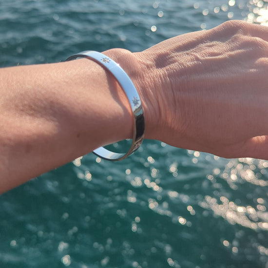 Sterling silver bangle worn on the wrist beside the sea