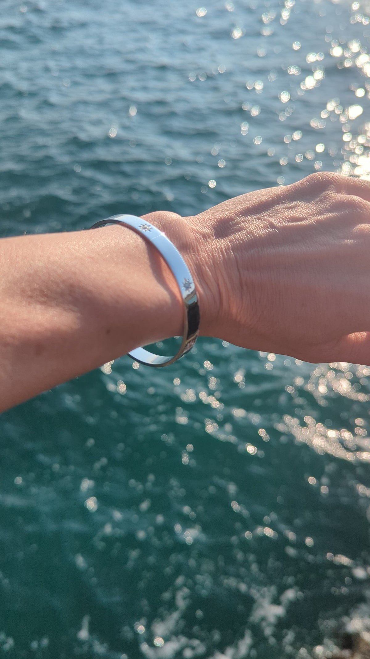 Sterling silver bangle worn on the wrist beside the sea