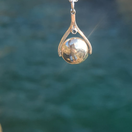 Video of silver spinning necklace with London blue topaz shimmering in the sunlight above the ocean made by Booblinka Jewellery.