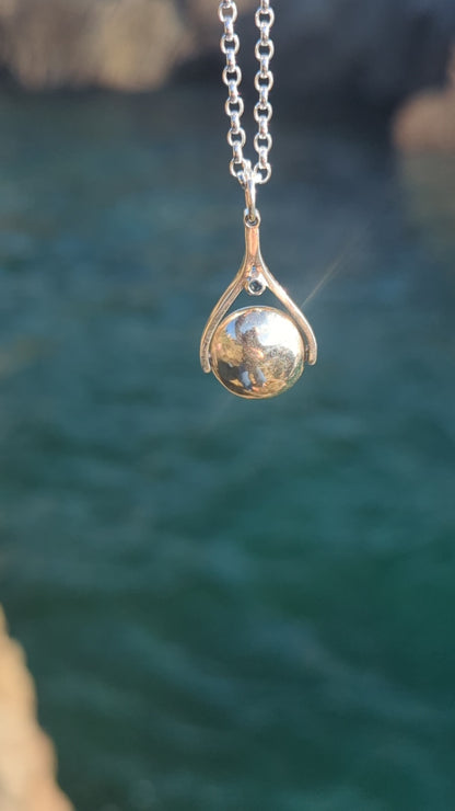 Video of silver spinning necklace with London blue topaz shimmering in the sunlight above the ocean made by Booblinka Jewellery.