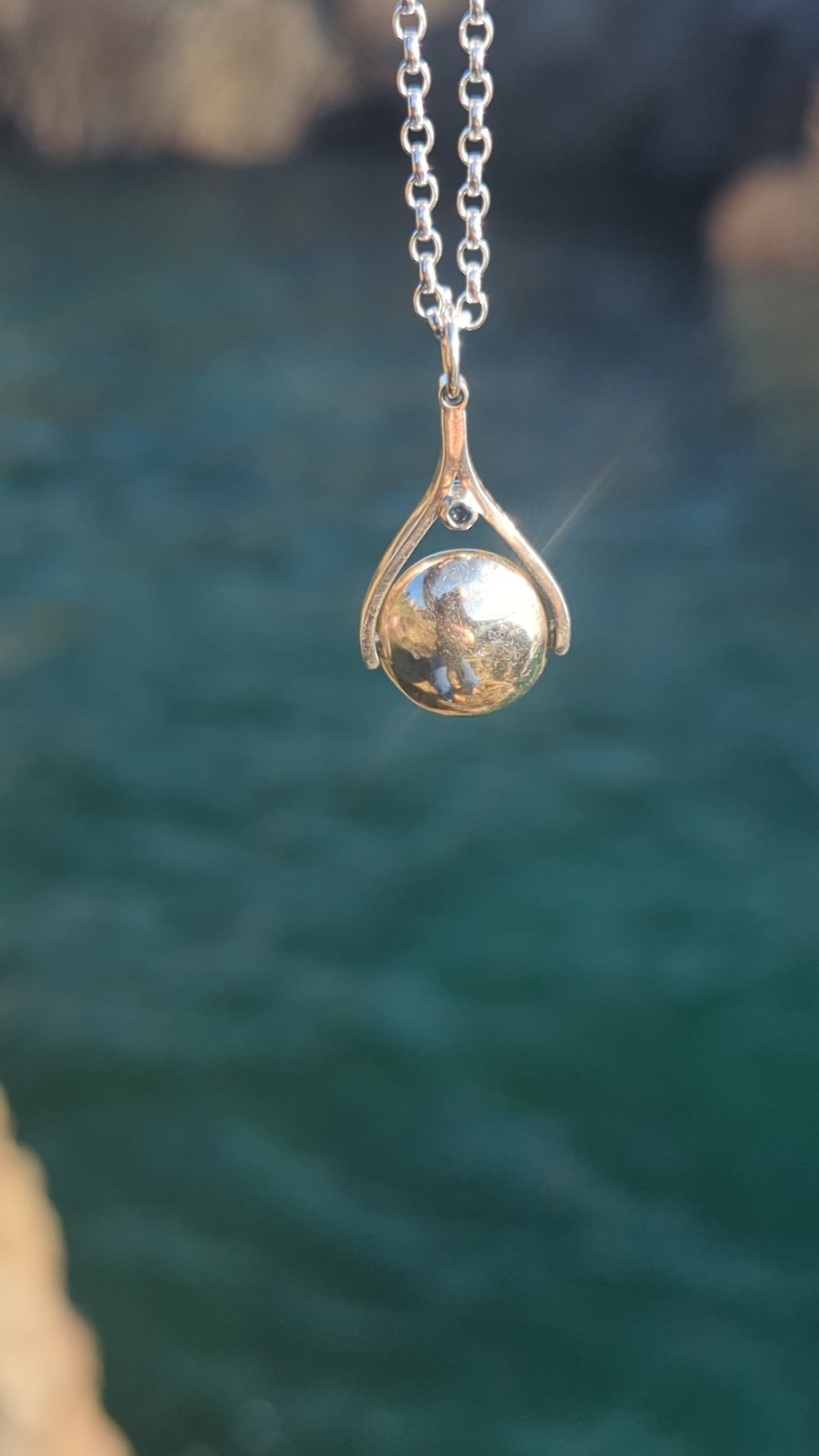 Video of silver spinning necklace with London blue topaz shimmering in the sunlight above the ocean made by Booblinka Jewellery.