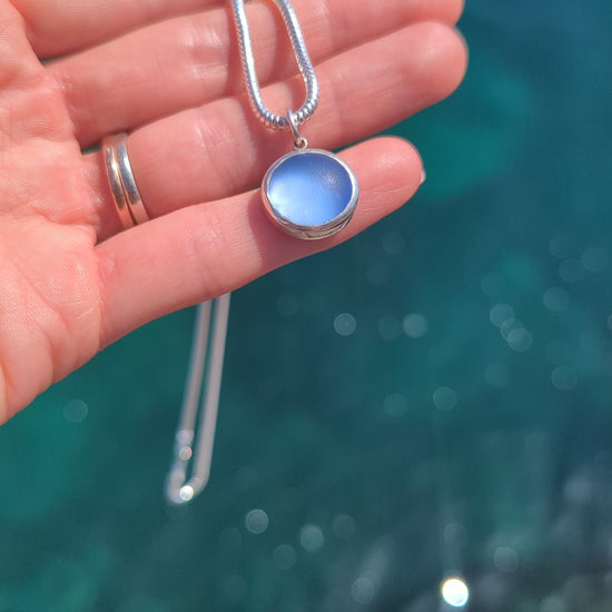 Close-up video of a blue sea glass pendant in sterling silver showing the colour above shimmering ocean.