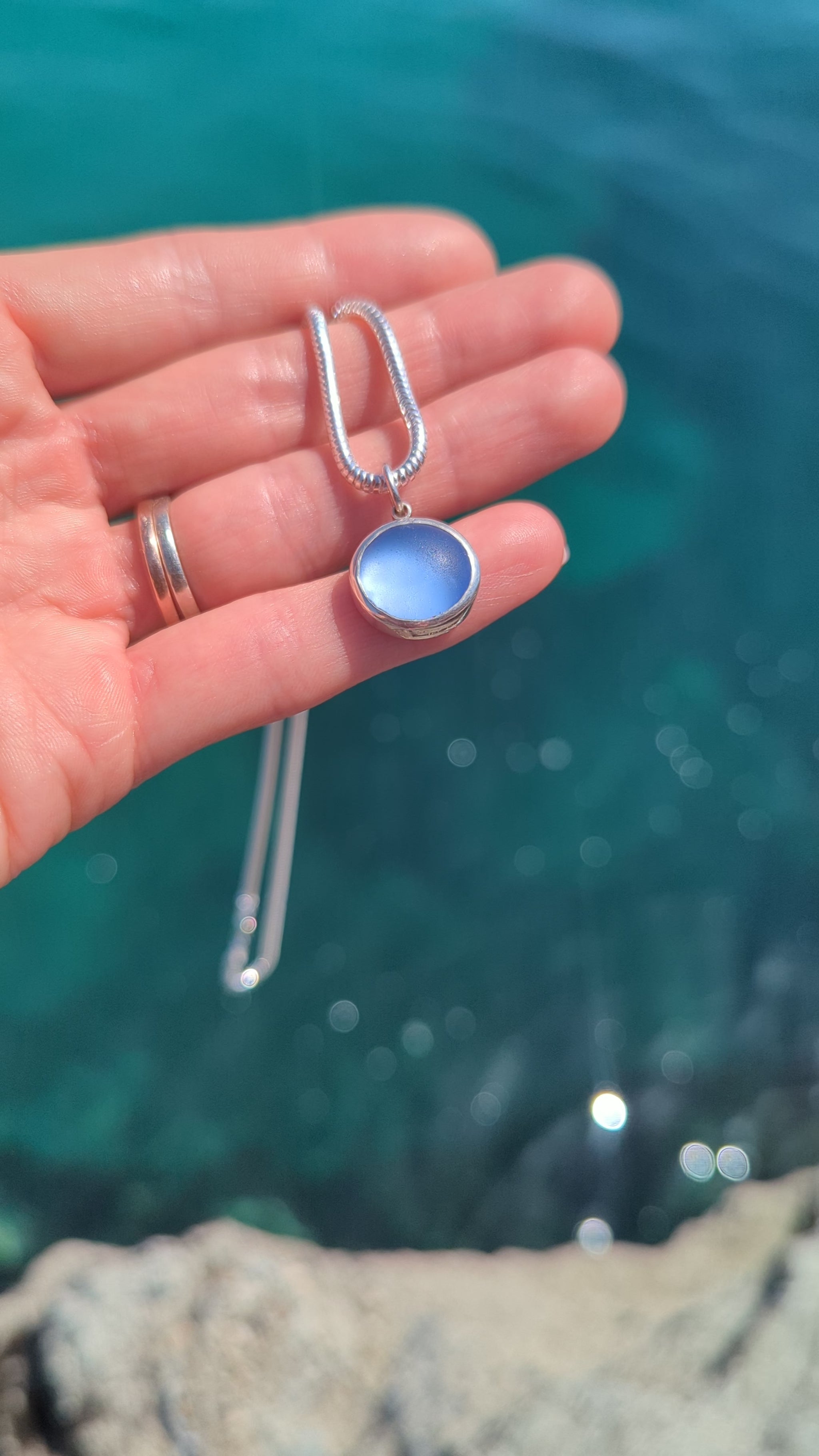 Close-up video of a blue sea glass pendant in sterling silver showing the colour above shimmering ocean.