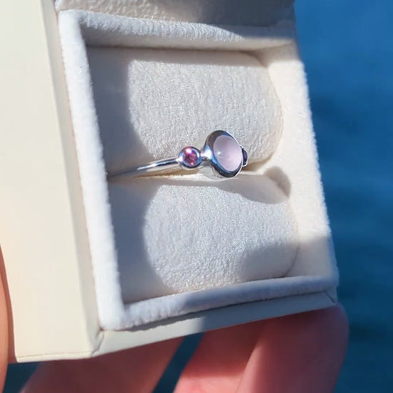 Silver ring with pink sea glass and pink tourmaline gemstones in an ivory jewellery box against a blue ocean made by Booblinka Jewellery
