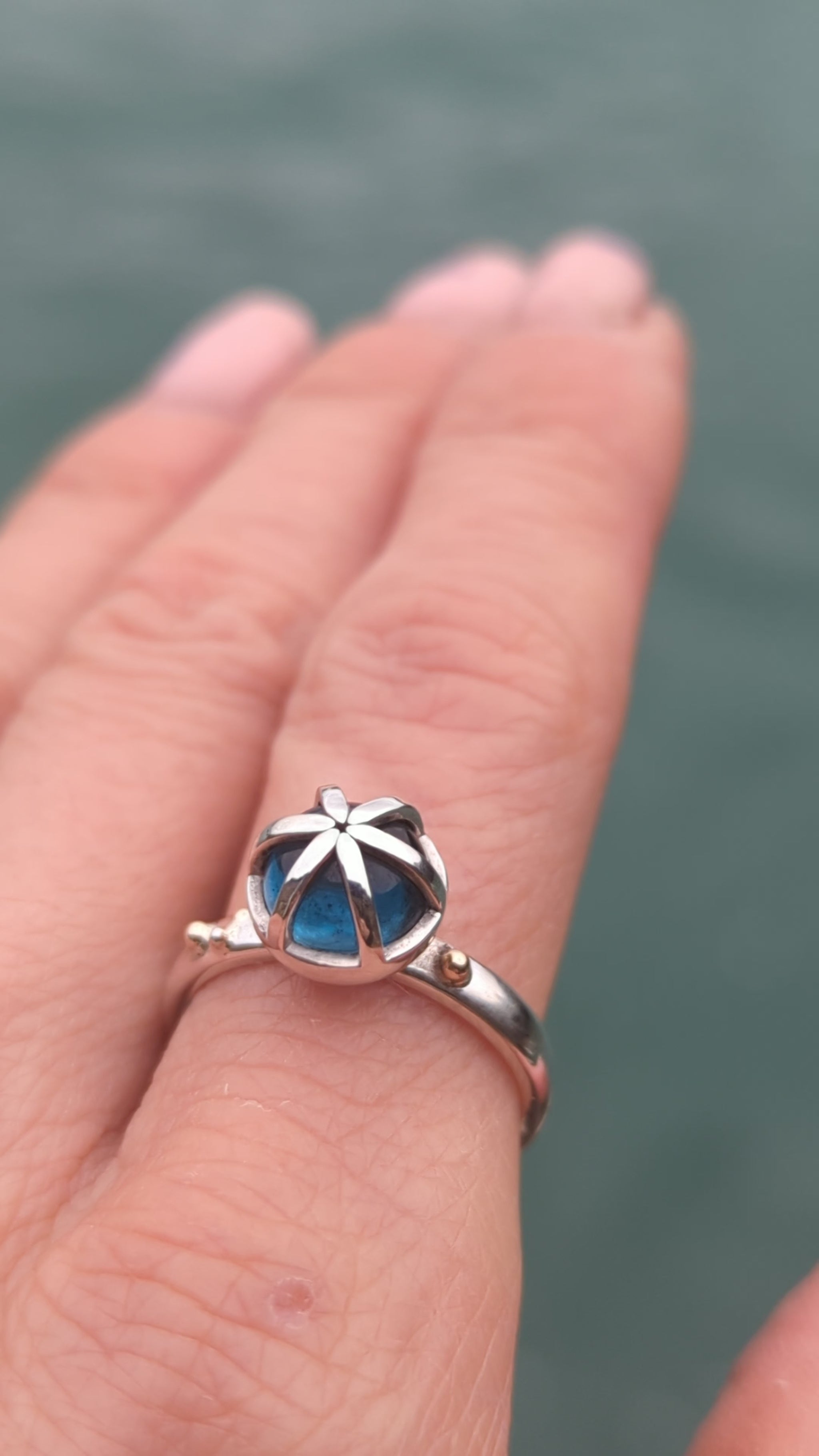 Video of a statement silver ring on a hand with round London blue topaz in a cage with gold granules made by Booblinka Jewellery.
