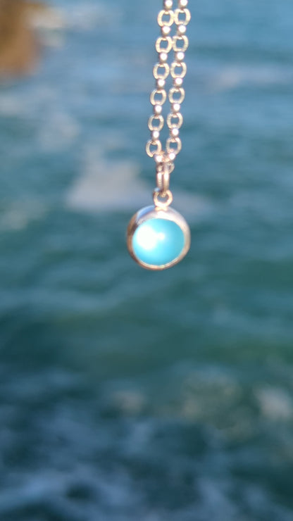 Blue round sea glass pendant in silver showing the full beauty above the ocean made by Booblinka Jewellery.