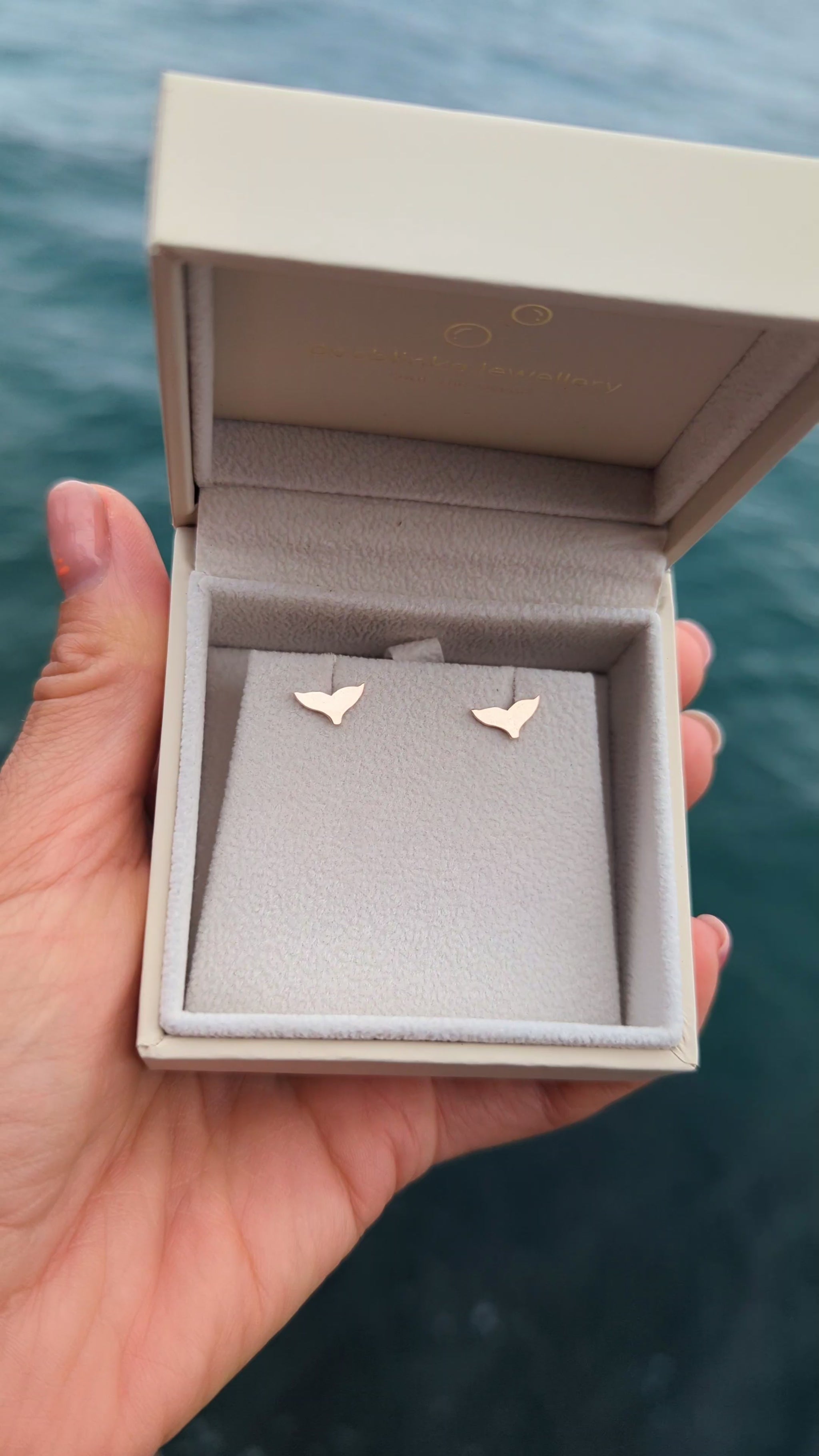 video of 9ct rose gold mermaid tail earrings in a jewellery box held above the ocean