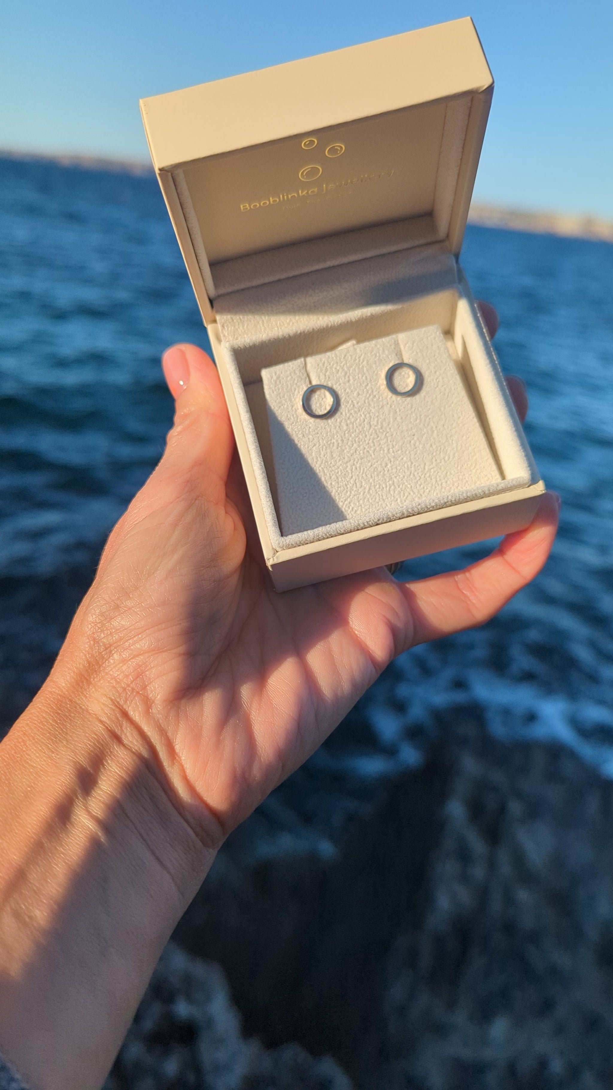 Video of  handmade 9ct gold circle stud earrings in a Booblinka Jewellery box held in hand above the ocean.