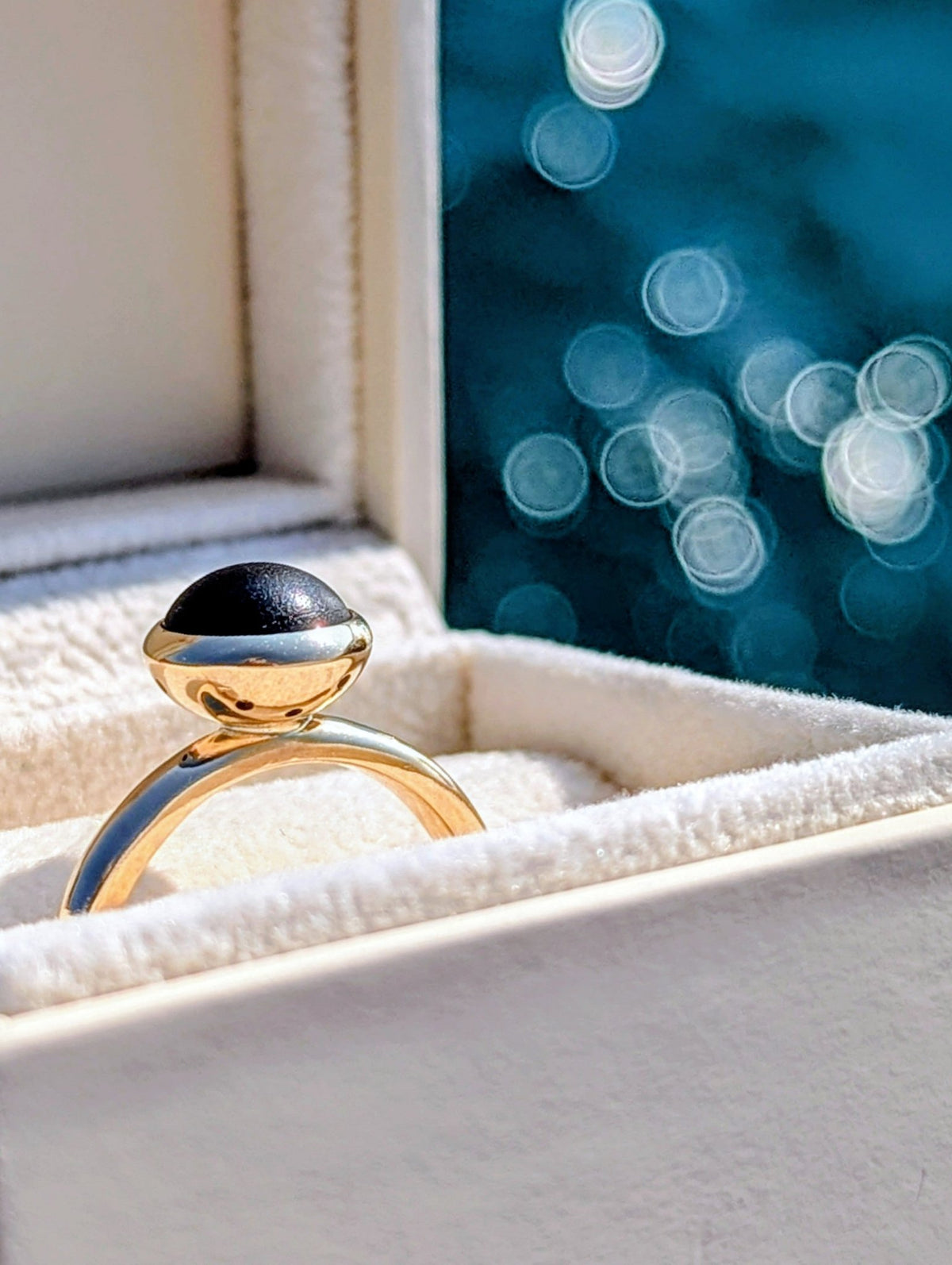 One-of-a-kind black sea glass ring in solid 9ct gold photographed beside the ocean in Cornwall