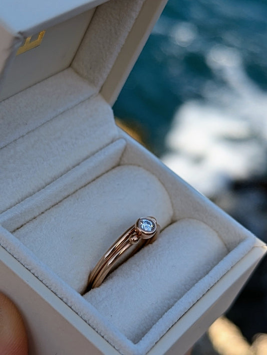 Rose Gold Solitaire Moissanite Stacking Rings – DEI Collection in a plush ivory jewellery box held above the ocean by Booblinka Jewellery