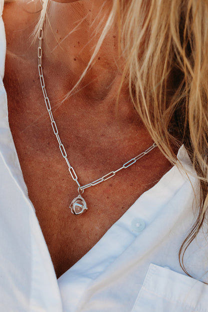Close-up of a silver ORB necklace worn on a woman's chest, with a pale pink rose quartz sphere on a paperclip chain.
