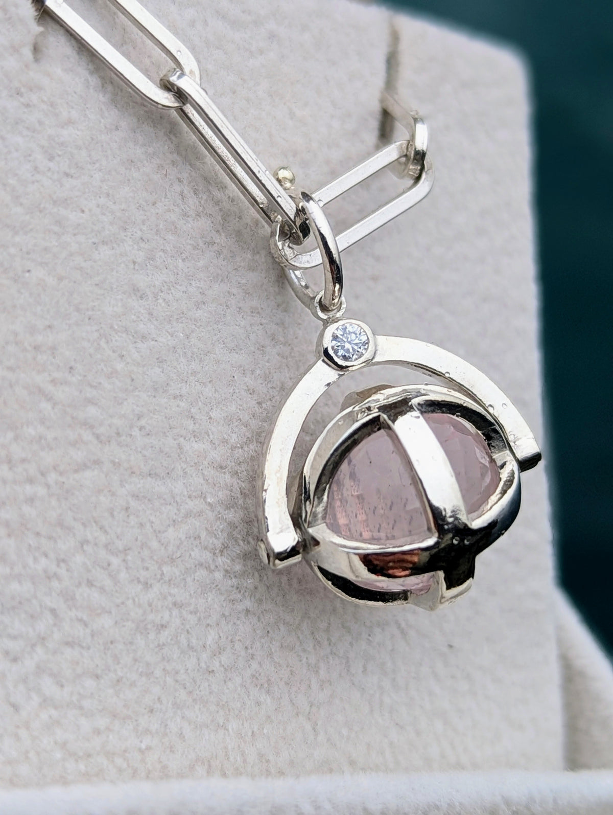 Close-up of a silver ORB spinning pendant with rose quartz and moissanie in an open jewellery box.