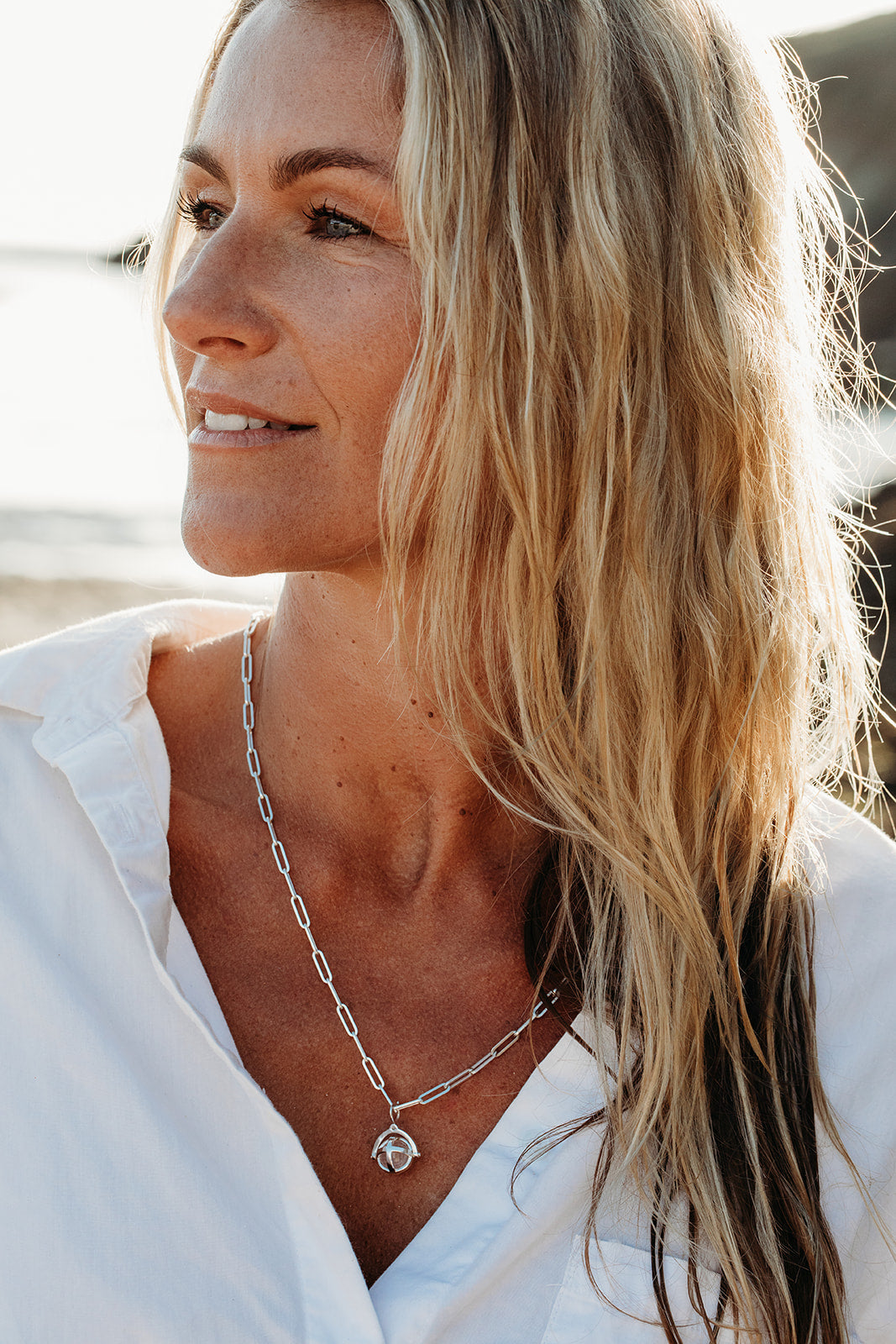 Blonde woman in a white shirt wearing a silver ORB necklace with a rose quartz sphere on a long paperclip chain.