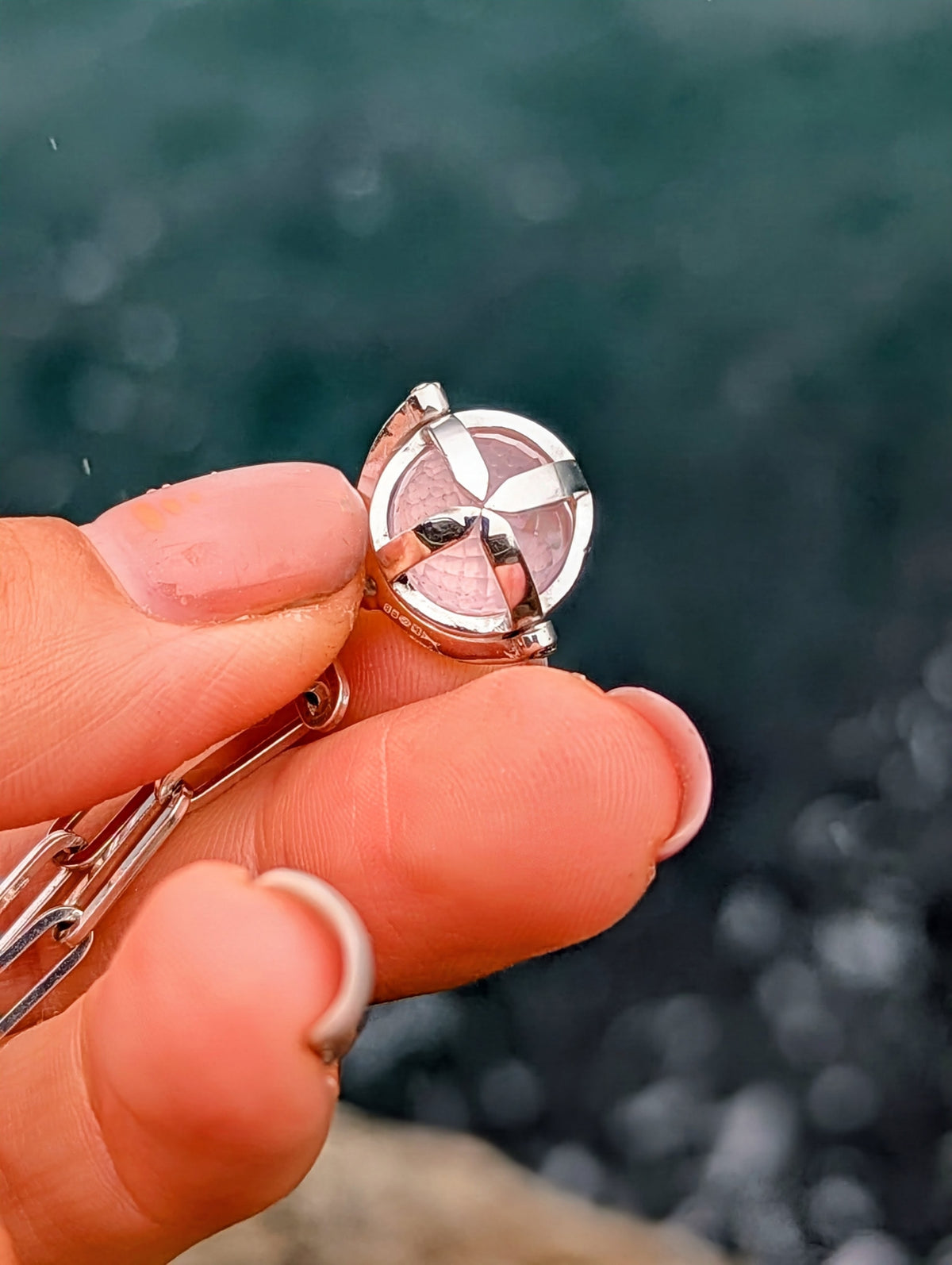 Close-up of a silver ORB spinning pendant held between fingers, showing the rose quartz sphere, silver cage and small moissanite.