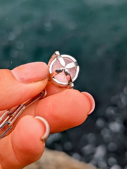 Close-up of a silver ORB spinning pendant held between fingers, showing the rose quartz sphere, silver cage and small moissanite.