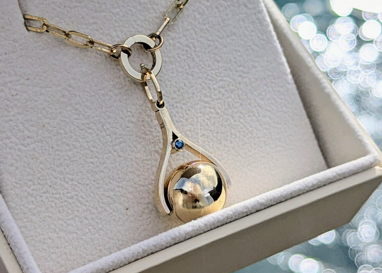 Spherical Spinning Necklace in Solid Gold with blue diamond in a jewellery box with shimmering ocean background - Personal or Memorial Jewellery made by Booblinka Jewellery