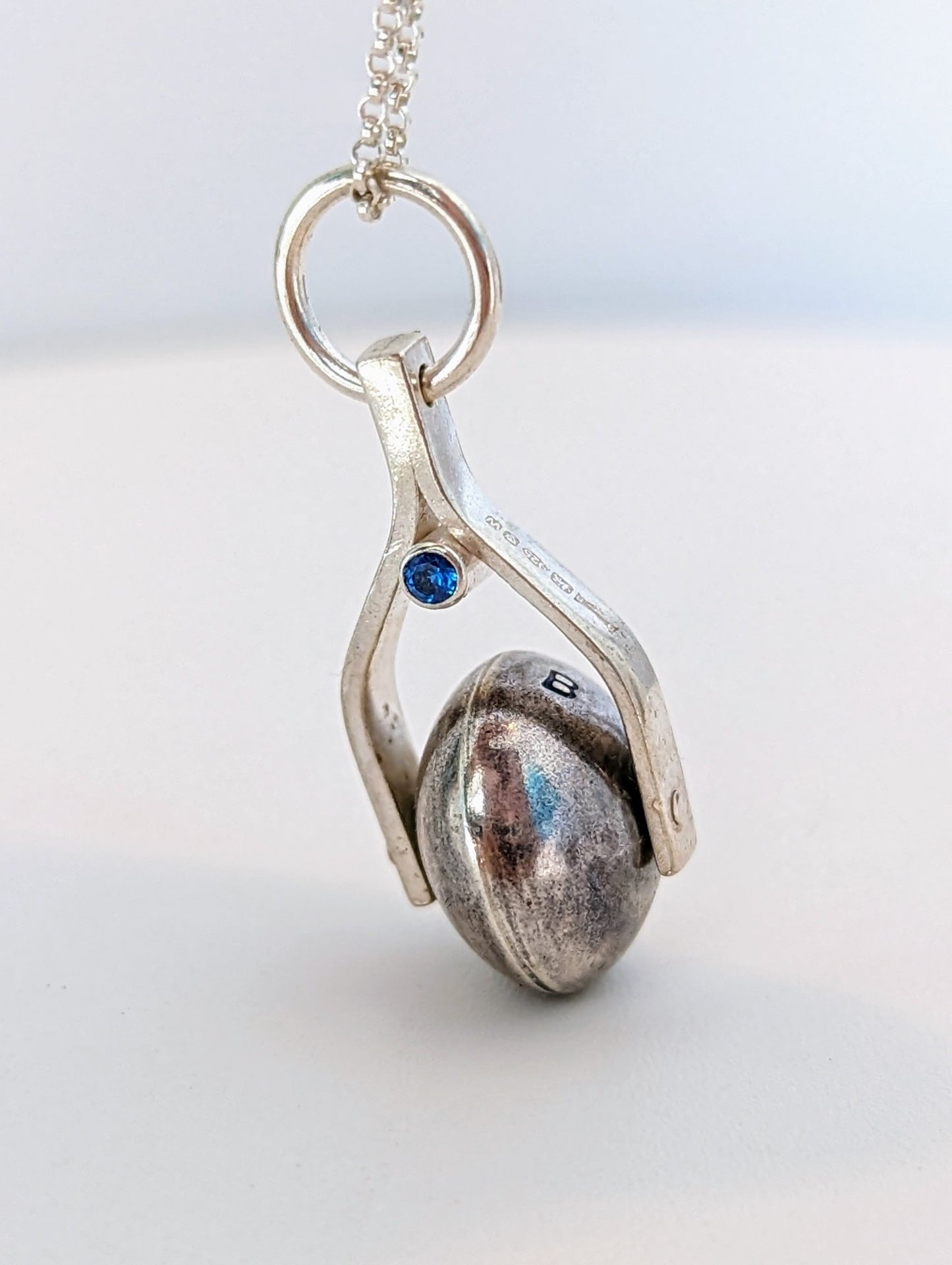 Detailed shot of the spinning moon necklace in sterling silver with a blue gemstone, showcasing its unique design as seen in 'Playing Nice' by Booblinka Jewellery 