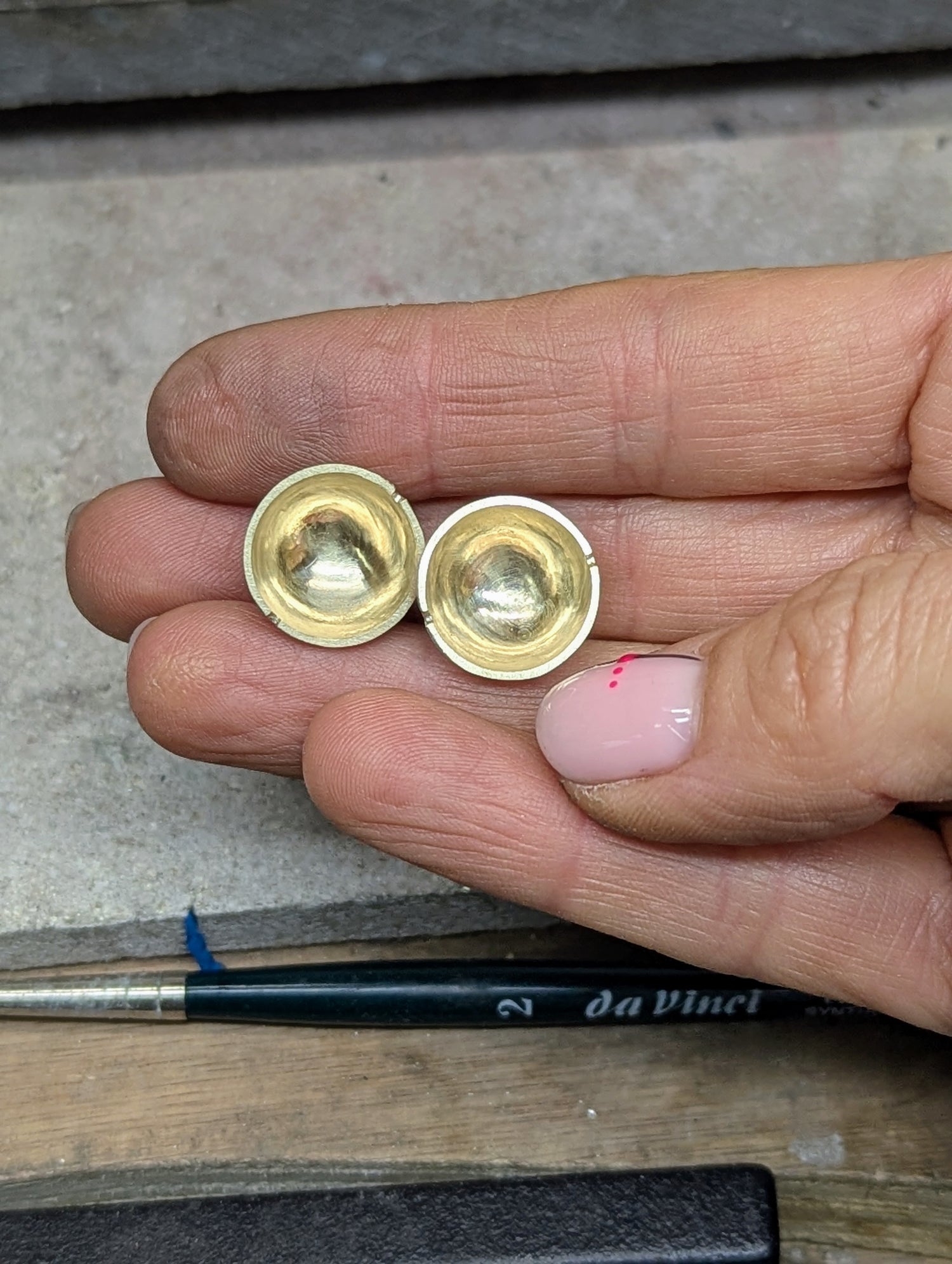 Two halves of a gold bead for a spinning pendant held between fingers on a jewellery bench