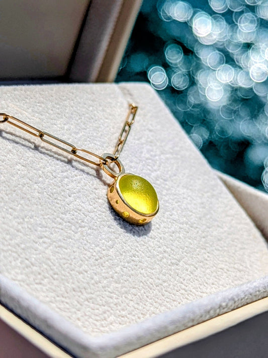 Gold paperclip necklace with round rare yellow sea glass in a jewellery box against blurred ocean background made by Booblinka Jewellery.