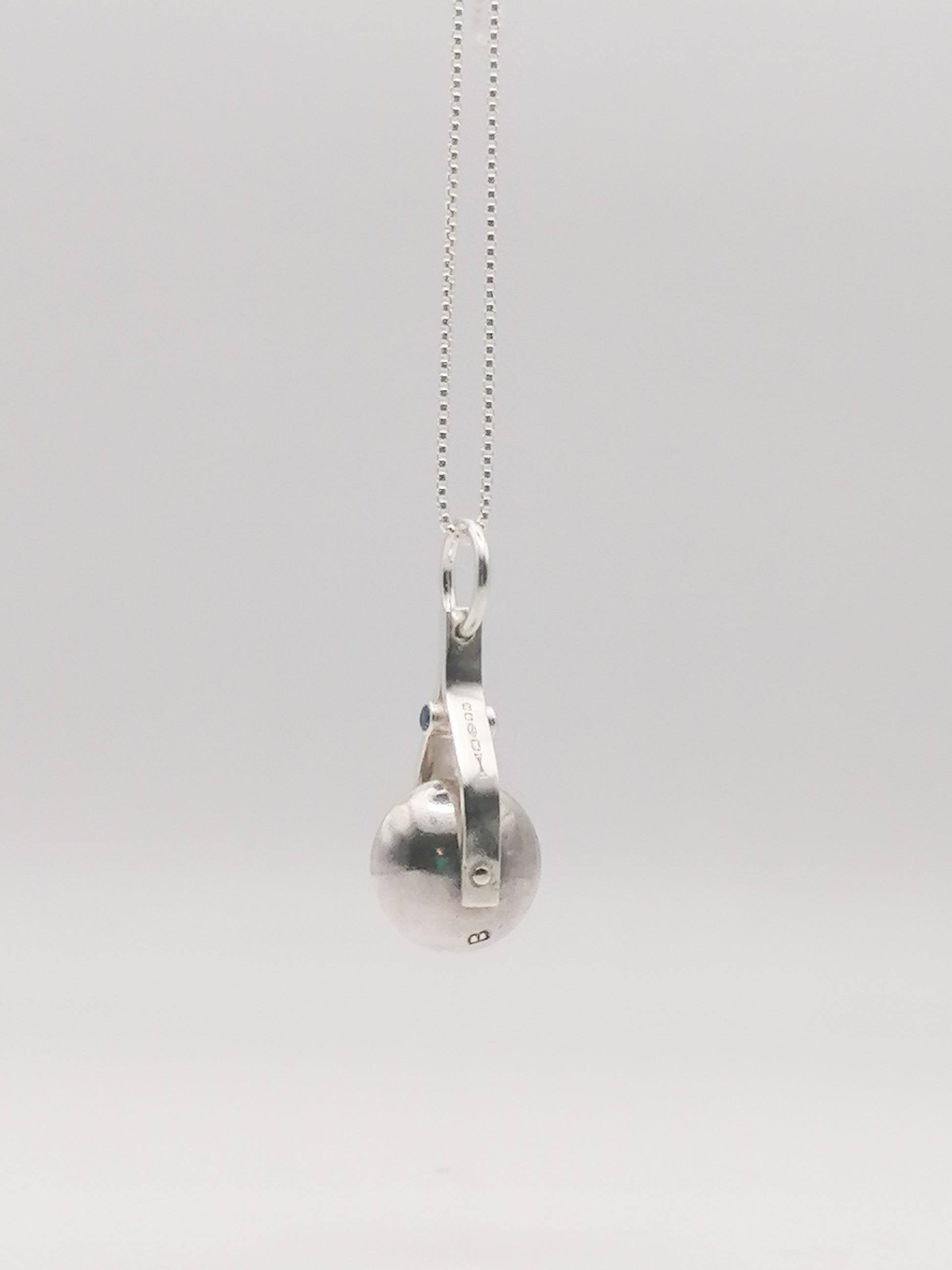 Shot of the spinning moon necklace in sterling silver with a blue gemstone, showcasing its unique design as seen in 'Playing Nice' by Booblinka Jewellery